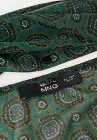 Groen gestreepte stof met bloemmotieven, een knoopsluiting en een zwart label met het merk "MNG" en maatinformatie.