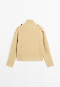 Beige ribbad tröja med hög krage, med en croppad passform och knappraccent på axlarna. Mjuk textur och avslappnad passform.