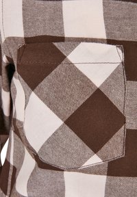 Camicia a quadri marrone e crema con tasca applicata. Il tessuto ha un aspetto texturizzato, con quadrati delineati in modo distinto e colori a contrasto.