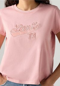T-shirt en coton rose clair à manches courtes, avec un logo brodé "Levi's 73" en design courbé sur la poitrine.