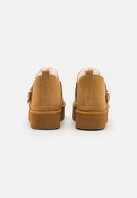 Ruskotuiset nilkkurit ruskeasta mokasta, joissa on litteat kumipohjat, karvavuori ja takanauha helppoon pukemiseen. Sivussa yksinkertainen metallinen solki.