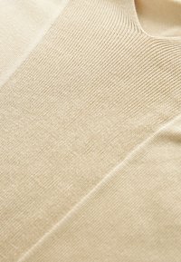 Vaaleanbeige neulekangas, jossa on hienovarainen pinta, V-pääntie ja sileä, pehmeä pinta. Ei näkyviä kuvioita tai koristeita.