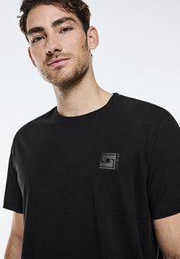 Sort bomulds T-shirt med rund hals og korte ærmer, med et diskret præget logo på venstre brystområde.