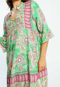 Vestido verde con estampado y acentos en rosa. Presenta diseños florales, un escote en V y mangas de tres cuartos con forma de campana. Tela ligera con una silueta fluida.