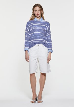 Maglione a righe blu e bianche in maglia con una vestibilità ampia, abbinato a pantaloni corti bianchi fino al ginocchio e sandali con tacco argentati.