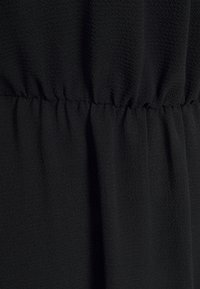 Černá látka s mírně texturovaným povrchem a nařaseným detailem. Hladký a splývavý design, vhodný pro různé styly oděvů.