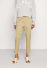 Beige chinos i bomull med rak ben design och knappstängning, kombinerade med en grå sweatshirt och beige klackmules.