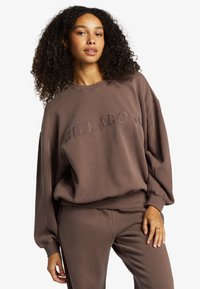 Hnedý sweatshirt Billabong s oversize rukávmi, rebrovaným výstrihom a spodným lemom, s embosovaným logom na prednej strane. Mäkký bavlnený materiál.