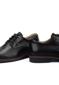 Chaussures en cuir noir avec une texture lisse, bout rond, lacets et logo subtil. Semelle en caoutchouc plate avec un léger talon.
