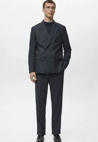 Costume bleu marine à deux rangées de boutons avec revers crantés, design minimaliste, pantalon slim et chaussures habillées noires. Finition en tissu lisse.