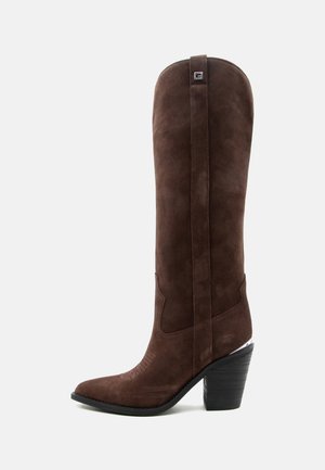 Stivale alto in pelle scamosciata marrone stile western con punta appuntita e tacco nero impilato su uno sfondo chiaro uniforme.