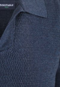 Marineblauwe gebreide pullover met een kraagontwerp. Heeft een geribbelde structuur en zachte stof. Label zegt "Suitable" nabij de halslijn.