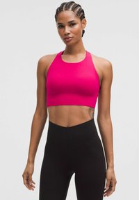 Sujetador deportivo rosa intenso con un escote alto y diseño de espalda de nadador, combinado con leggings negros de cintura alta. Textura suave, forma ajustada.