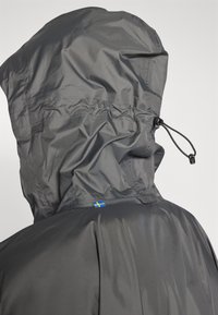 Veste imperméable grise avec capuche à cordon de serrage, texture lisse et petit drapeau suédois bleu et jaune au dos.