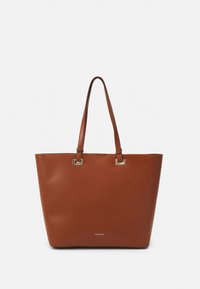 Brązowa torba na ramię wykonana z gładkiego materiału, z dwoma długimi uchwytami i złotymi kwadratowymi akcentami w miejscach mocowania. Minimalistyczny design.