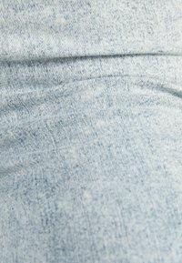 Lähellä oleva vaaleansininen farkkukangas, josta näkyy yksityiskohtainen rakenne ja ompeleet sekä kevyet rypyt.