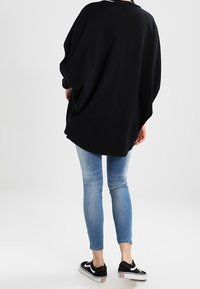 Svart oversized topp med rund halsringning, parat med ljusblå smala jeans och svarta sneakers. Slät textur, avslappnad fall.