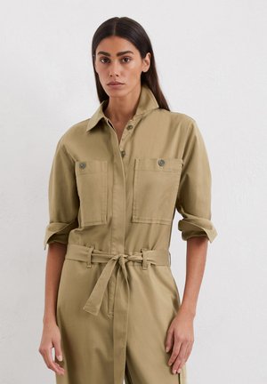 Hellbrauner Utility-Overall mit zwei Brusttaschen, Knopfverschluss, hochgekrempelten Ärmeln und einem gebundenen Taillengürtel. Glatte Stoffstruktur.