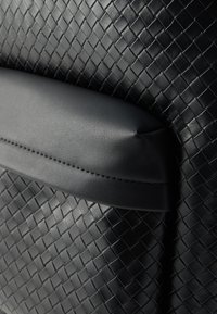 Cuir noir tressé avec une poignée noire lisse. La texture présente un motif en losanges, créant un aspect structuré et moderne.