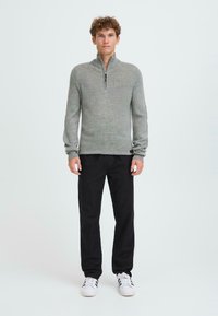 Lys grå zip-up genser med ribbet tekstur, kombinert med svarte bukser og hvite sneakers. Enkelt, praktisk design med høy krage.