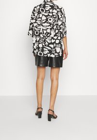 Musta-valkoinen lyhythihainen paita, jossa erilaisia abstrakteja kuvioita, yhdistettynä mustiin nahkashortseihin ja remmikkäisiin korkokenkiin.