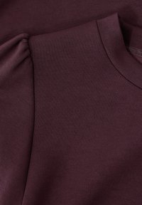 Lähikuva tummasta purppuranvärisestä vaatteesta, jossa on kokoontunut puffihihna ja ribattu pyöreä kaula-aukko, joka näyttää kankaan tekstuurin.