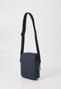 Navy blue crossbody bag with a square shape, made of textured fabric, featuring a black adjustable strap and zip closure.