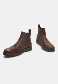 Bottines Chelsea en cuir marron avec des panneaux élastiques sur les côtés, bout rond et finition texturée. Semelle en caoutchouc à profile bas avec motif de crampons.