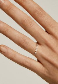Anillo de plata con un diseño delicado que presenta múltiples piedras pequeñas y transparentes dispuestas en una línea continua. Mano con acabado de uñas naturales mostrada.