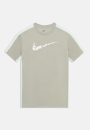 Světlé šedé sportovní tričko s krátkým rukávem, bílé proužky na bocích a bílý logo Nike ve tvaru křivky na hrudi s pixelovým efektem.