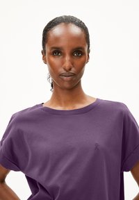 Paarse oversized katoenen T-shirt met korte mouwen en een geribde ronde hals. Heeft een klein geborduurd logo op de linkerkant van de borst.