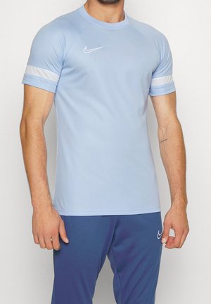 Mann trägt hellblaues kurzärmeliges Sportshirt mit weißem Streifen an den Ärmeln und blaue Hose, beide mit weißen Nike-Logos.