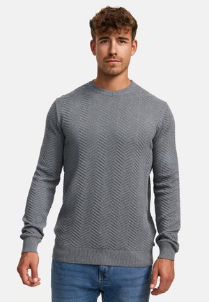 Grau gestrickter Pullover mit einem strukturierten Fischgrätmuster, Rundhalsausschnitt und gerippten Bündchen und Saum. Kombiniert mit blauen Jeans.