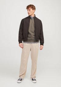 Zwarte bomberjack, groene pullover, gestreepte shirt, crèmekleurige broek en zwarte sneakers. De stof lijkt glad met een casual ontwerp.