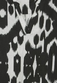 Mustavalkoinen kuvioitu kangas, jossa on abstrakti muotoilu epäsäännöllisillä muodoilla ja V-pääntiellä. Rakenne on kevyttä ja tekstuuriltaan miellyttävää.