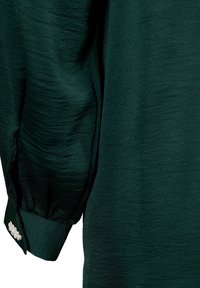 Manche longue vert foncé avec tissu texturé et boutons de manchette décorés de petites perles blanches.