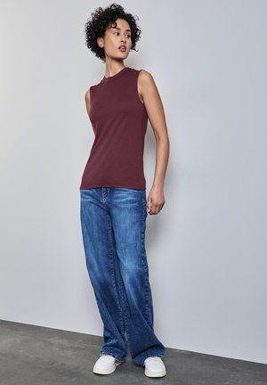 Bordeaux ærmeløs top parret med lysvaskede, brede jeans. Jeansene har et klassisk fem-lomme design og en lige snit.