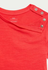 Camicia rossa a maniche corte con scollatura tonda e dettagli a bottoni sulle spalle. Realizzata in un tessuto morbido e texturizzato. Etichetta M&S visibile.