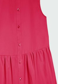 Vaaleanpunainen mekko, jossa on napitettava etuosa, pleatattu helma ja sileä pinta. Napit ovat kiiltäviä ja tasaisesti sijoitettu sauman varrella.