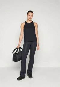 Črn brezrokavnik, prilegajoč, v kombinaciji s črnimi širokimi legicami. Model drži črno torbico z dvojno zanko. Gladke, mat teksture.