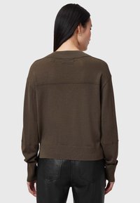 Maglione lavorato a maglia marrone con una vestibilità ampia, colletto a coste e maniche lunghe. Il tessuto sembra morbido con una texture liscia. Abbinato a pantaloni neri.