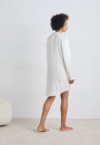 Abito da notte leggero a maniche lunghe in tessuto texturizzato bianco sporco, con colletto e vestibilità morbida, che arriva a metà coscia.