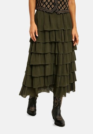 Mujer que lleva una falda de capas verde oliva oscura con botas de vaquero negras que tienen un bordado floral ligero.