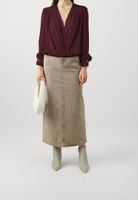 Blusa avvolgente bordeaux con maniche lunghe e spalle a sbuffo; gonna midi in denim beige con cuciture verticali; stivali alla caviglia grigi chiari a punta; borsa bianca.