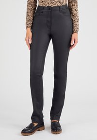 Pantalones negros de corte slim con una textura suave, que presentan una cintura alta, bolsillos frontales y un lazo para cinturón. Combinados con mocasines negros.