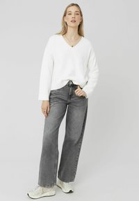 Pull-over blanc à col en V avec des manches larges, associé à un jean gris taille haute à jambes larges et des baskets blanches. Détails en tissu texturé visibles.