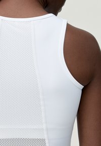 Top atletico bianco senza maniche con una texture perforata sul retro, caratterizzato da un tessuto morbido, un collo tondo e spalline sottili.