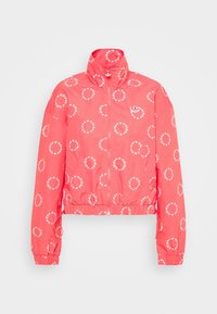 Korallfärgad kort jacka med uppstående krage. Har vita cirkulära loggor överallt och elastiska ärmar. Slät textur, lätt material.