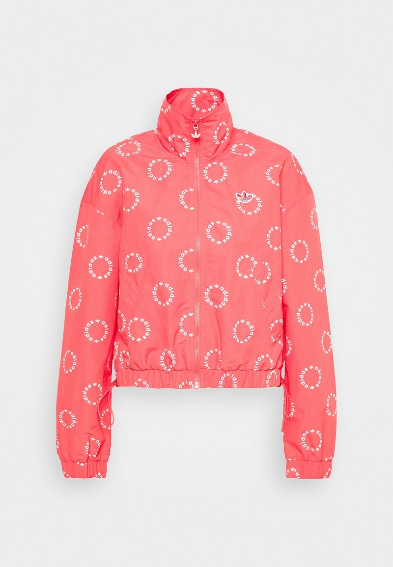 Korallfärgad kort jacka med uppstående krage. Har vita cirkulära loggor överallt och elastiska ärmar. Slät textur, lätt material.