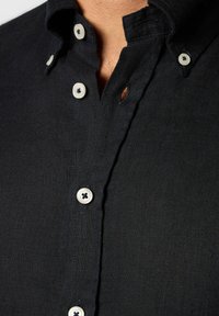 Camicia nera a maniche lunghe in tessuto testurizzato, con bottoni bianchi e colletto con placca di bottoni.